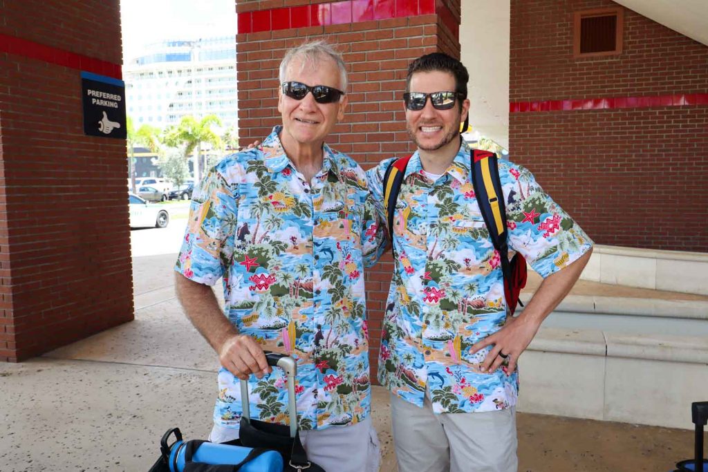 An older and younger man smiling and dressed in matching Disney cruise shirts. 