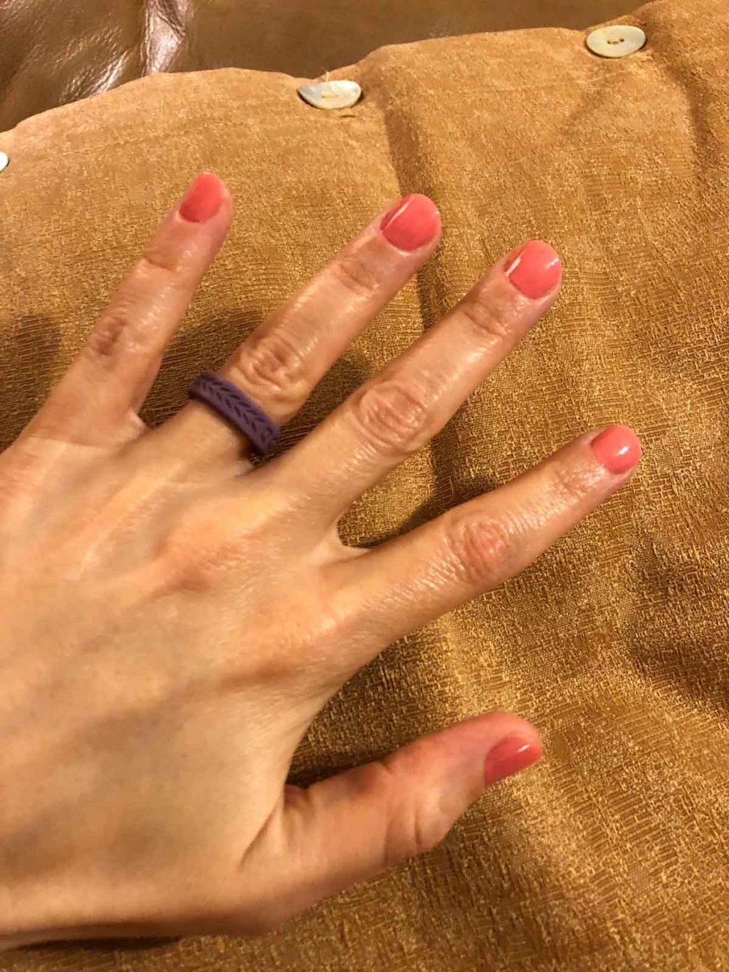 A woman's hand with painted pink nails and a purple qalo ring. 