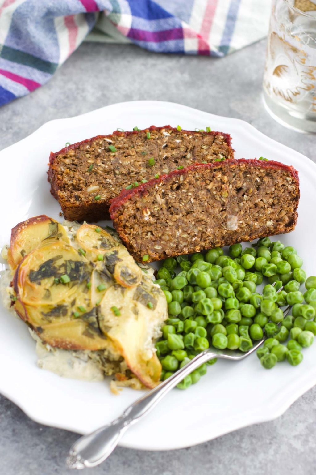 Two slices of mushroom loaf next to peas and scalloped potatoes on a white plate. 