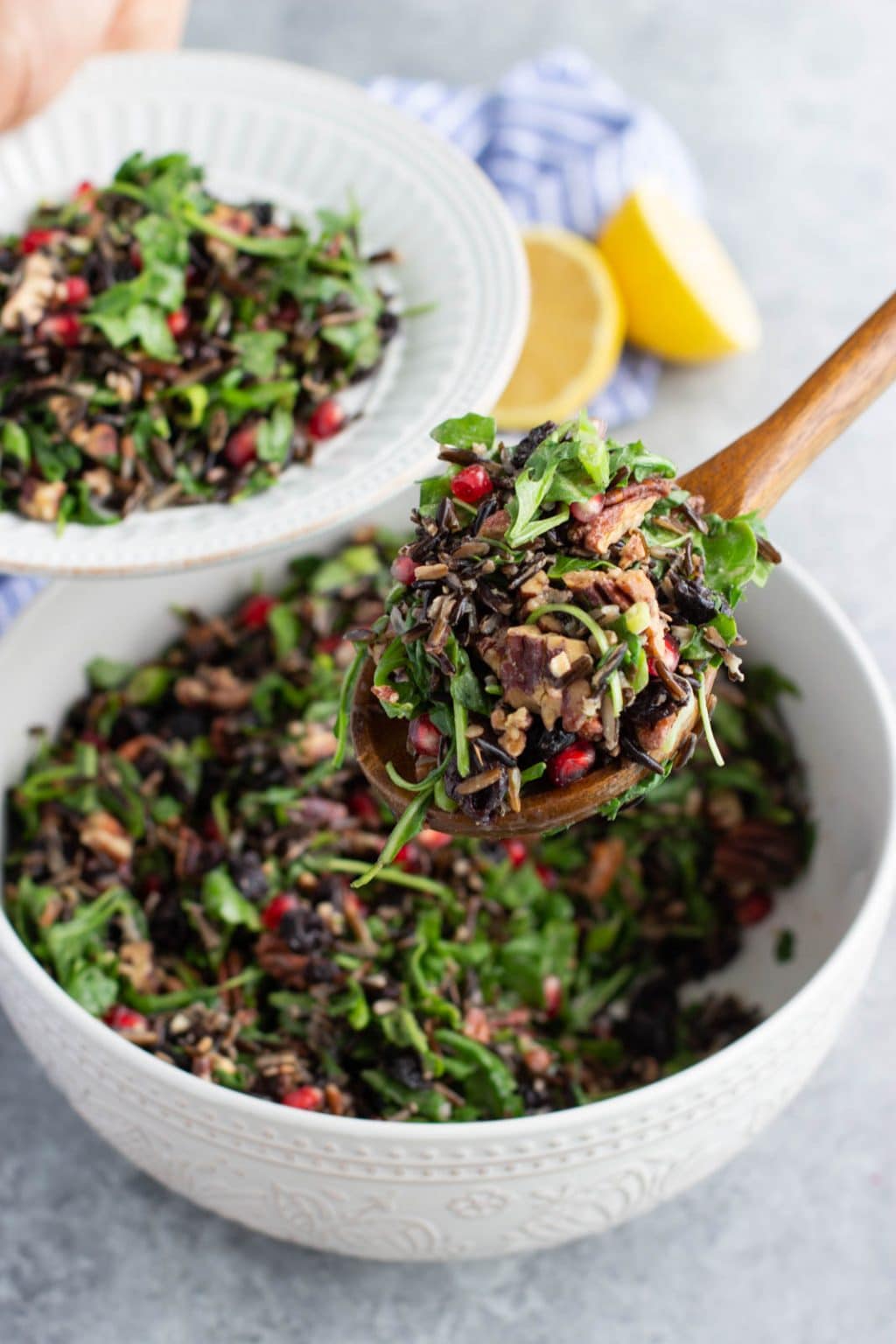 A wooden spoon scooping the salad out of a white bowl onto a smaller white plate. 