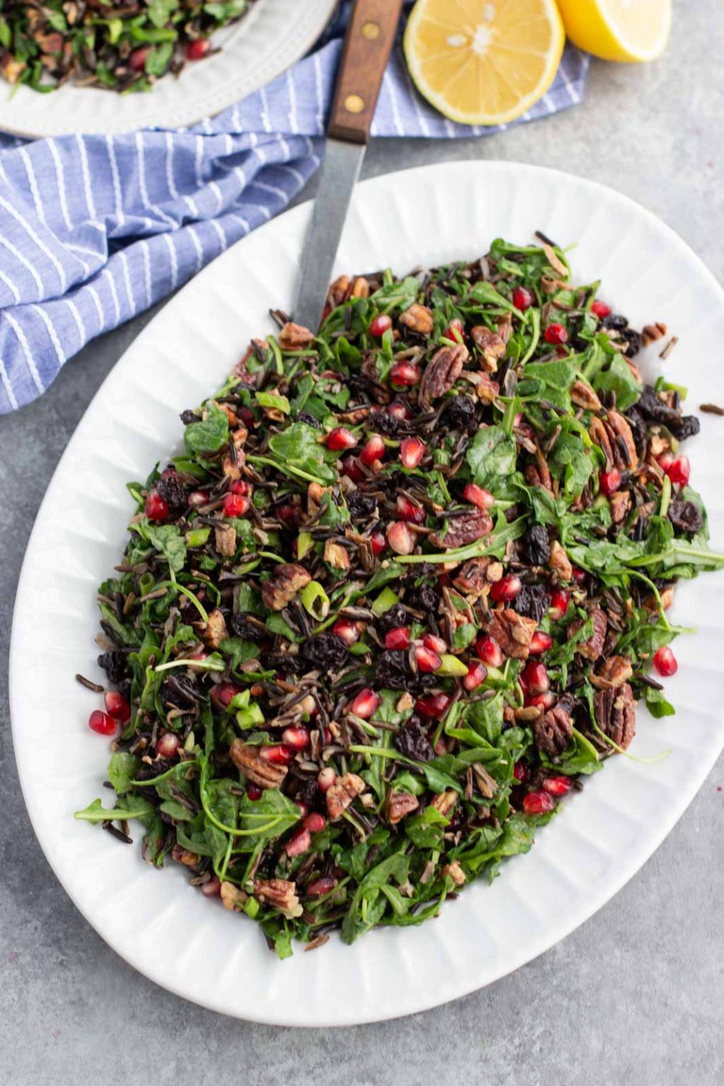 A large white platter filled with vegan Christmas salad and a serving spoon on a gray background.