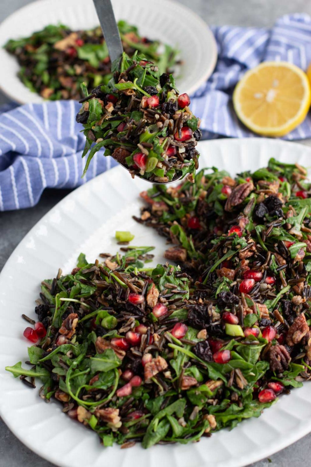 A spoon scooping salad from a large white platter on a gray background.