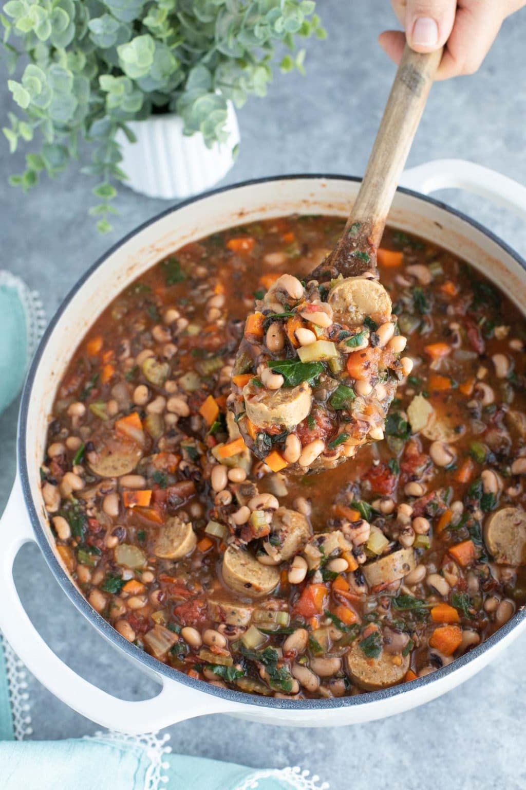 A hand holding a wooden spoon in a pot filled with soup on a gray background.