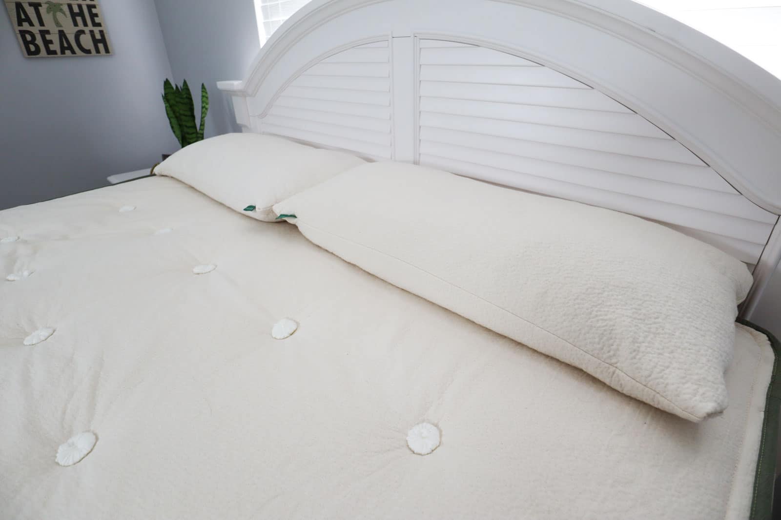 A bare mattress with two king pillows sitting top of it next to a white headboard. 