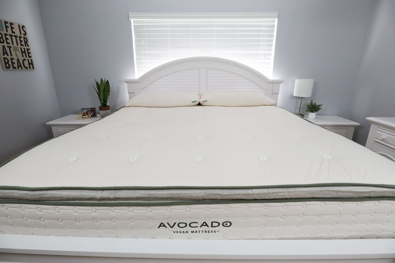 An Avocado Vegan Mattress on a white bed frame in a gray bedroom. 