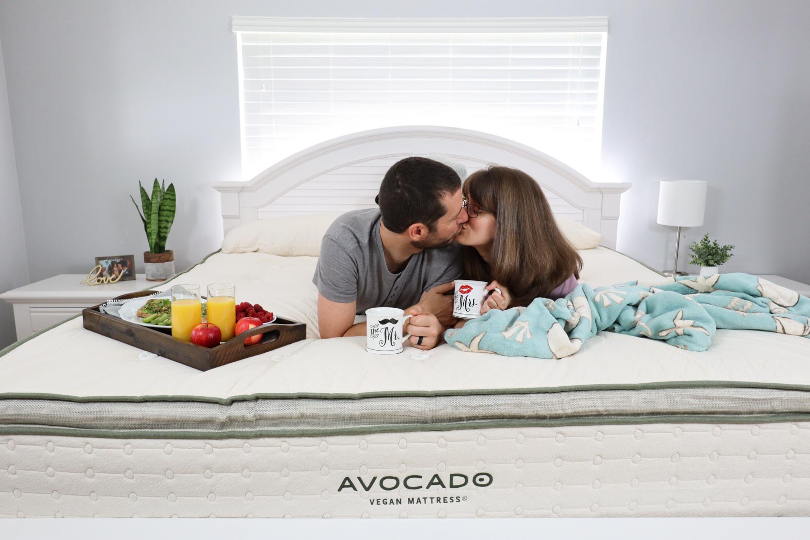 A man and woman kissing on top of an Avocado vegan mattress in a bedroom.