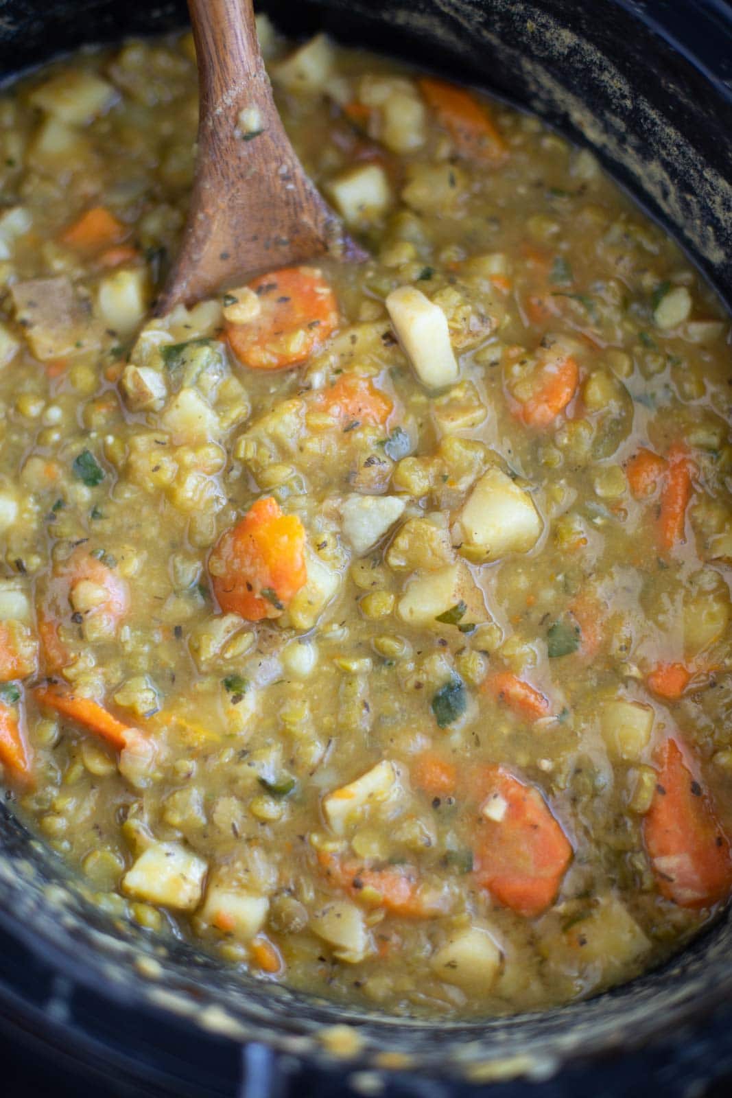 A black slow cooker filled with soup and a wooden spoon. 