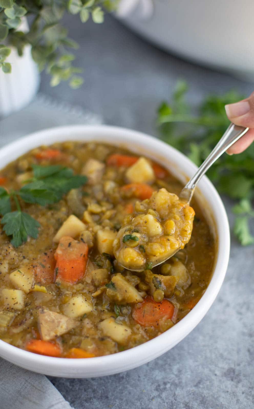 A hand holding a spoonful of soup over a white bowl on a gray background.