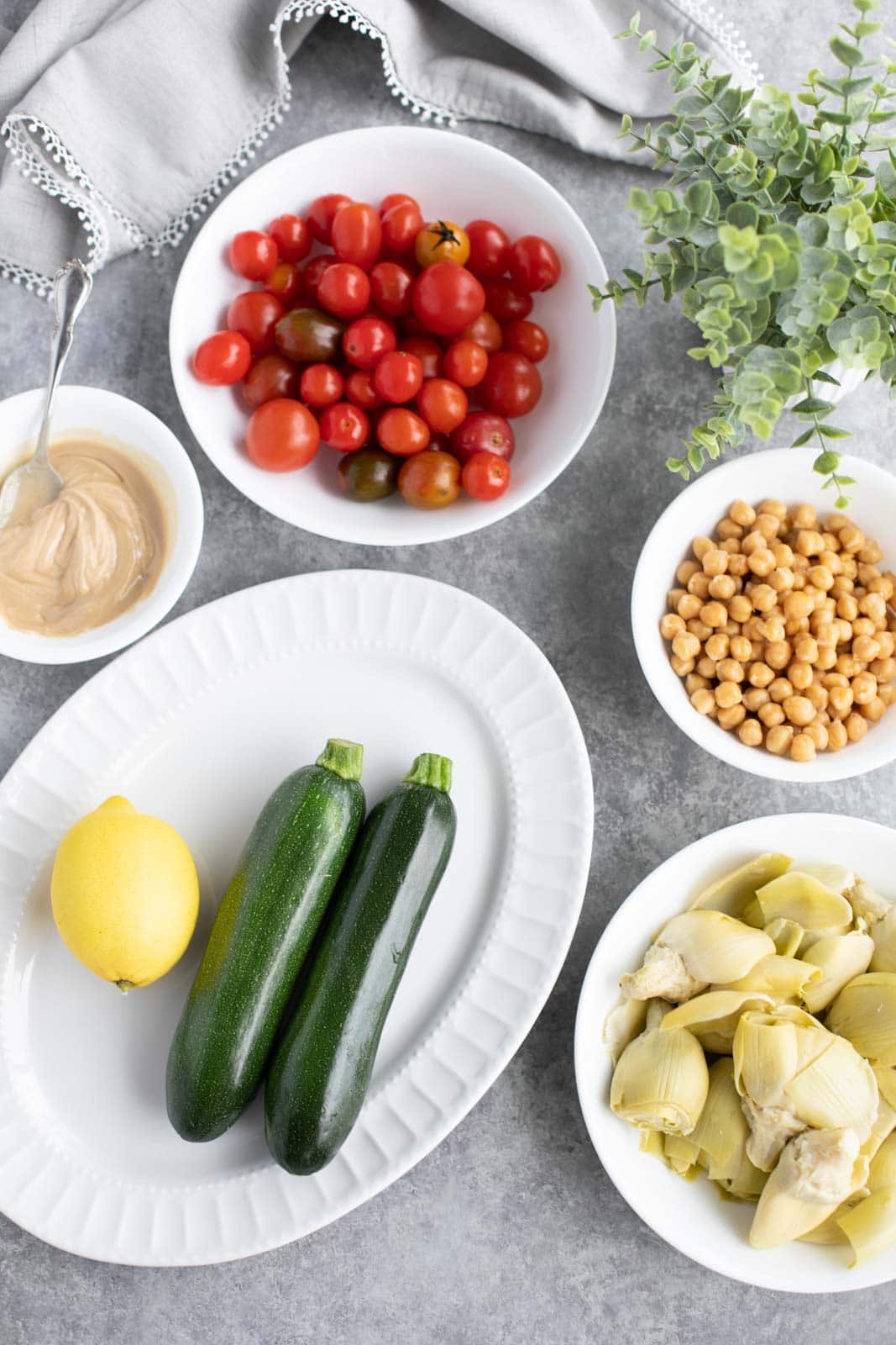 All the ingredients needed to make courgette salad on white plates with a gray background.