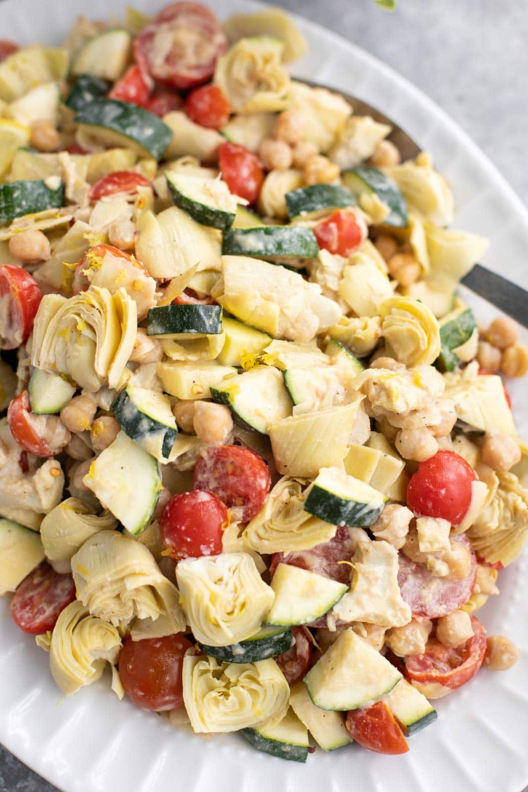 Courgette, tomatoes, artichokes and chickpeas on a white platter.