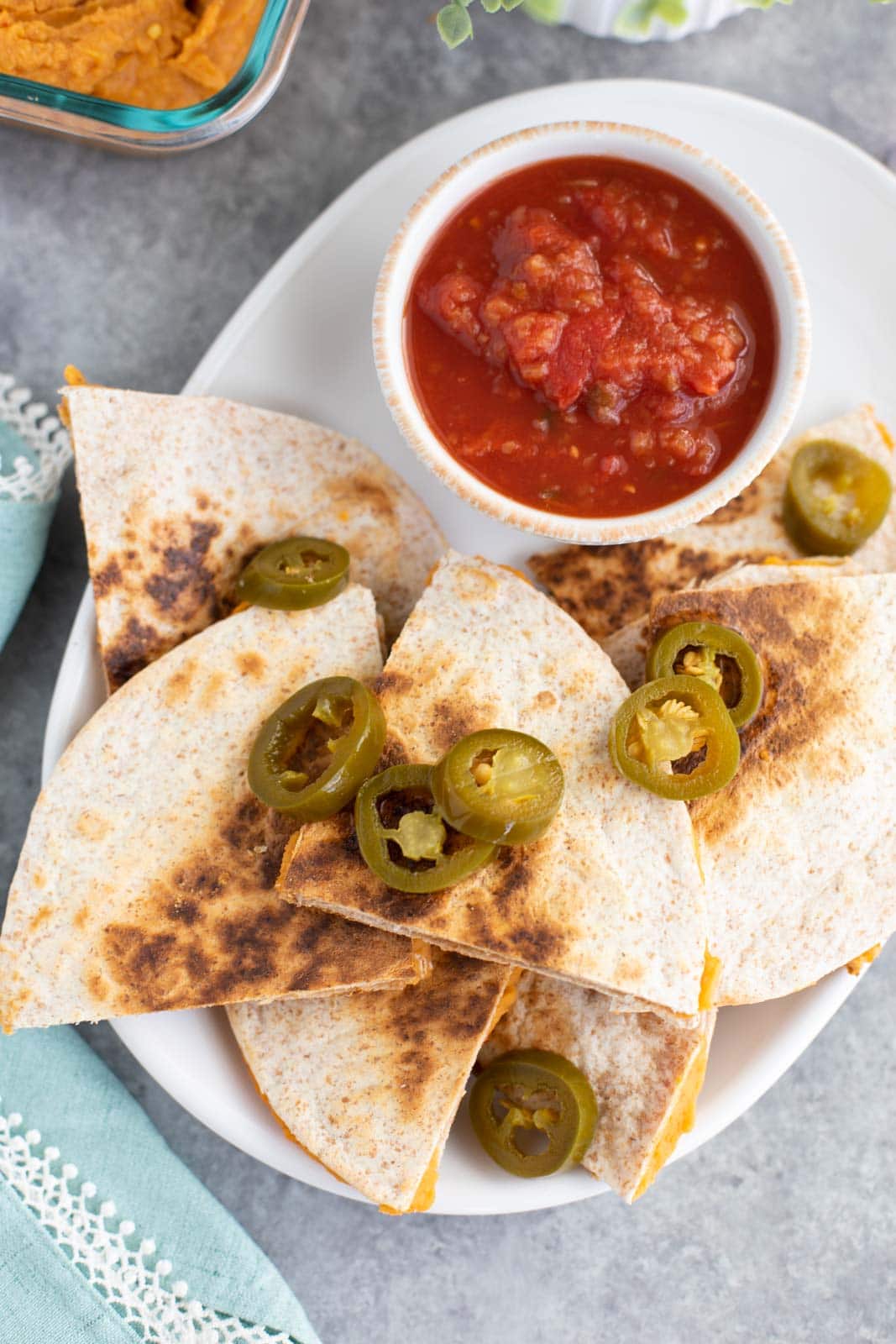Multiple quesadilla slices topped with jalapeños on a white plate with a bowl of salsa.