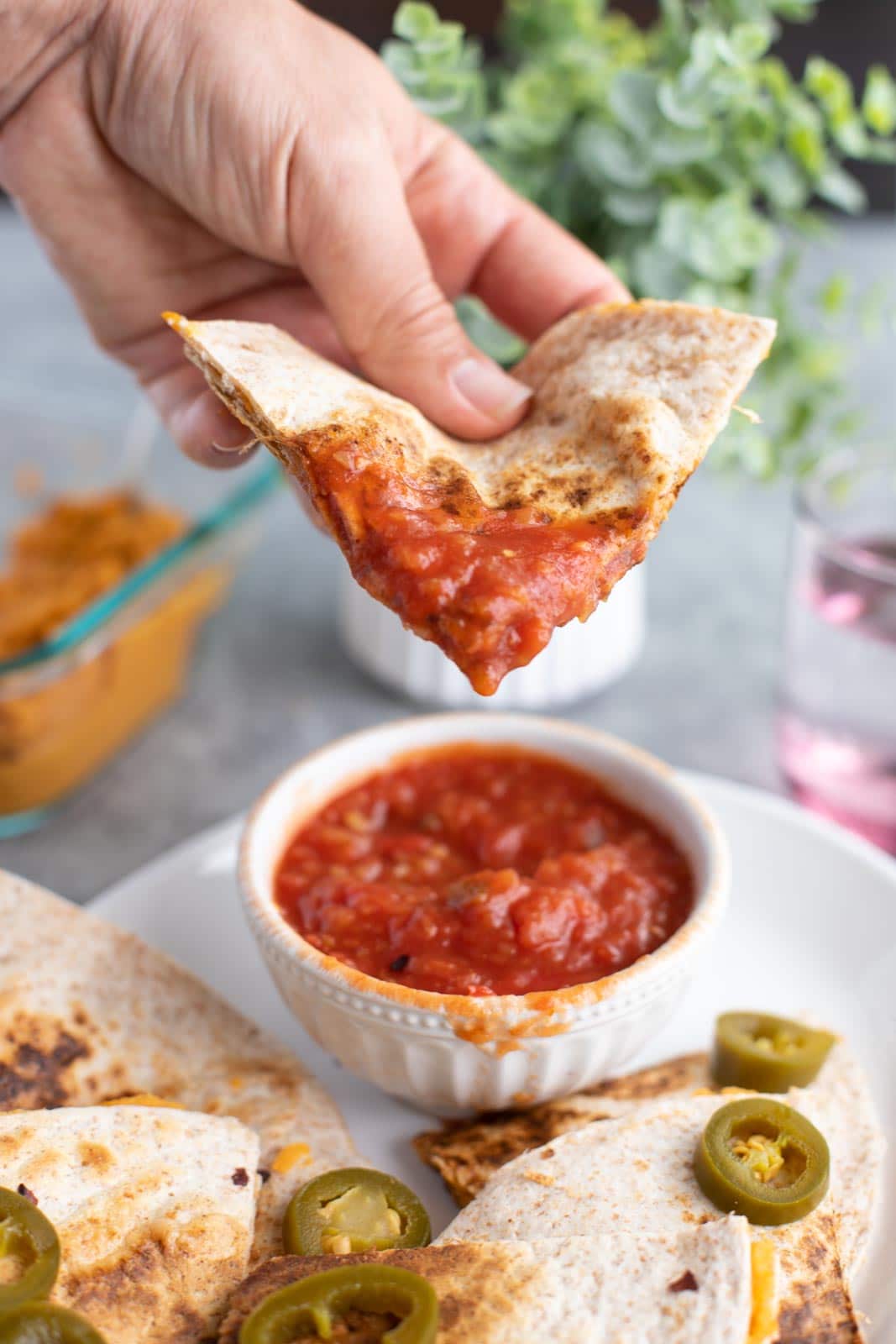 A hand dipping a quesadilla slice into a bowl of salsa.