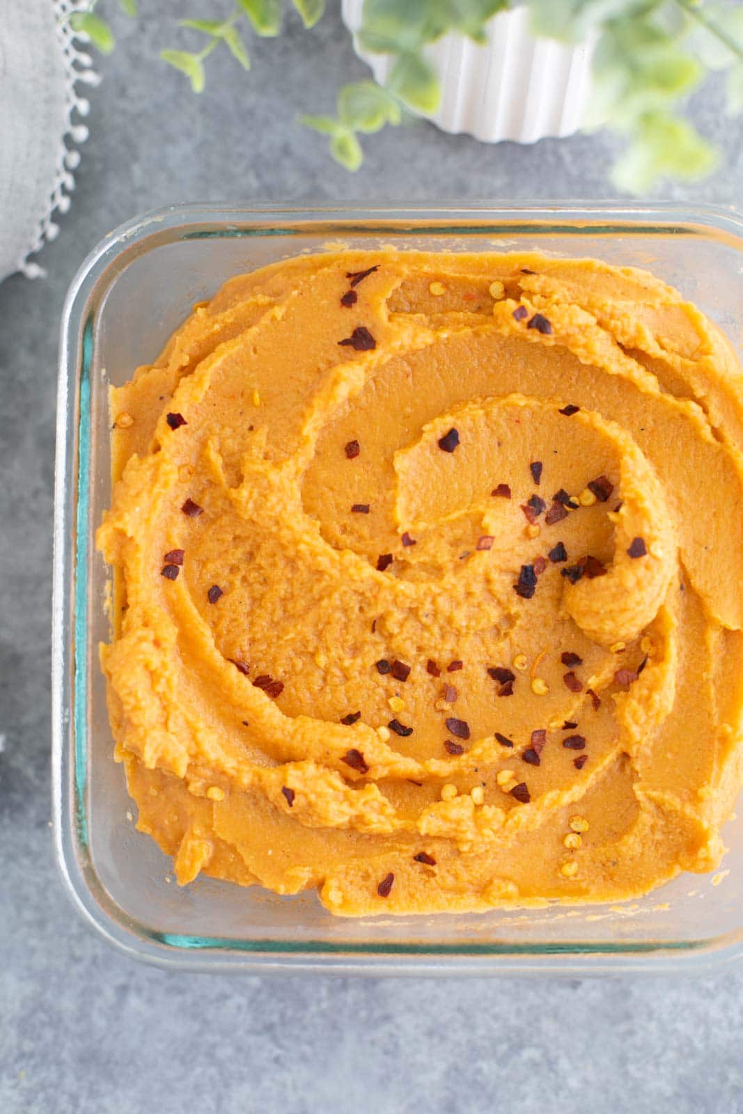Roasted red pepper hummus in a glass bowl on a gray background.