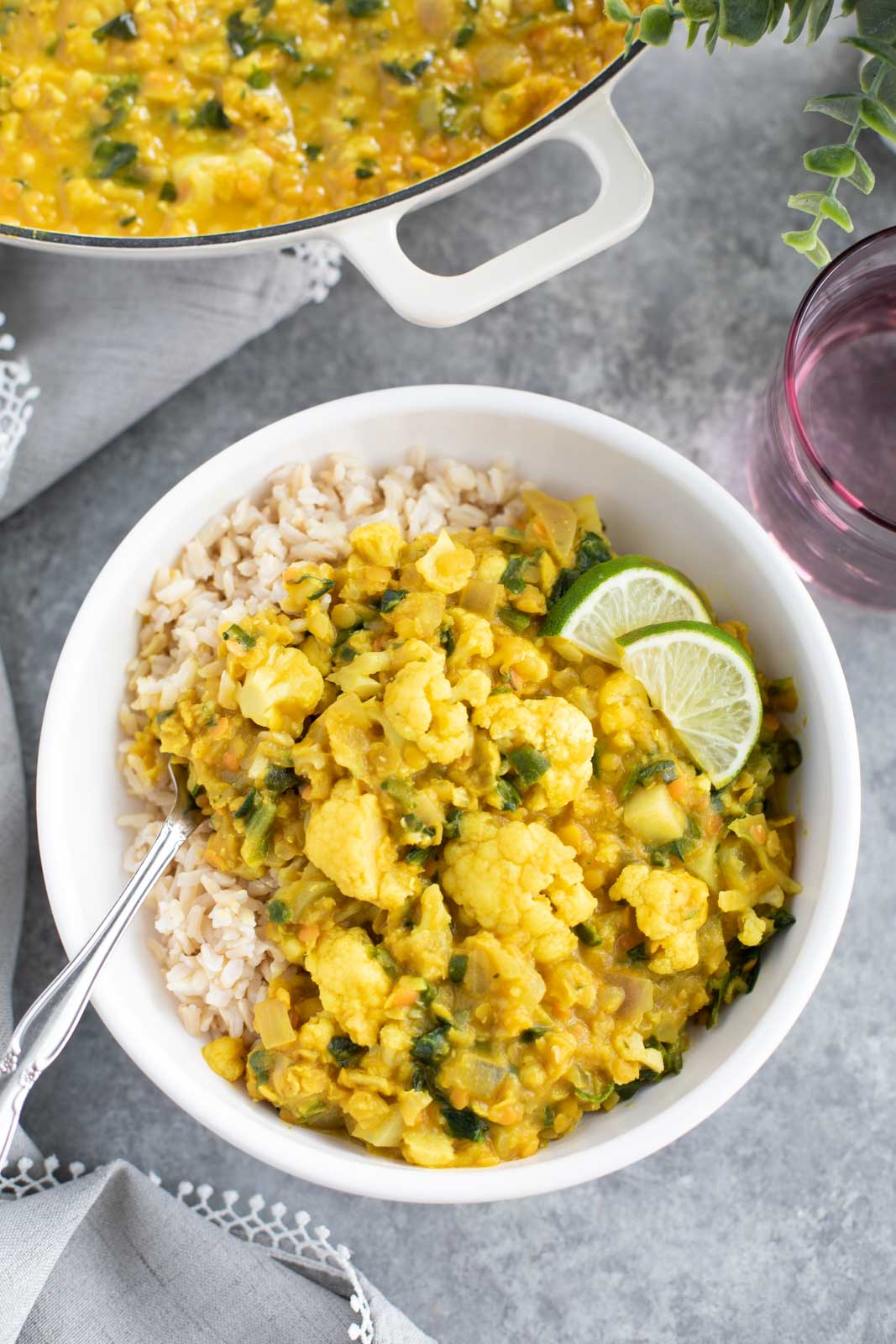 A white bowl filled with cauliflower curry and a fork on a gray background.