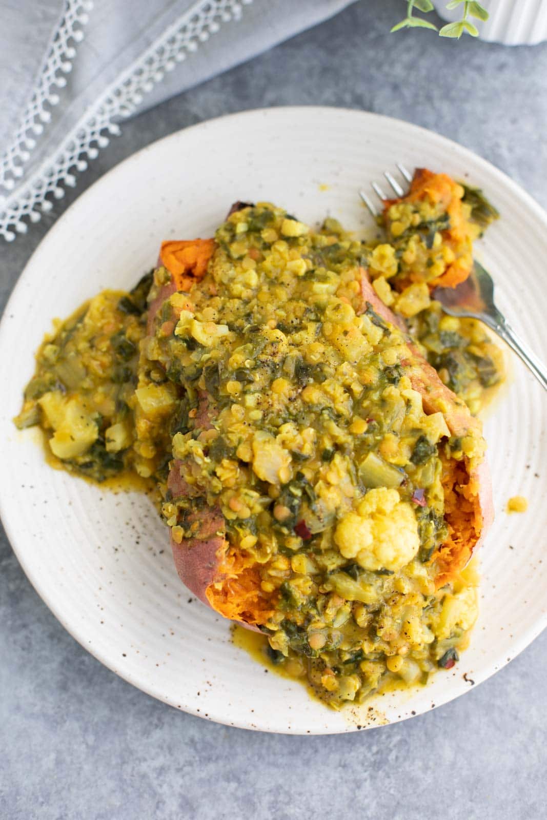 A roasted sweet potato topped with cauliflower curry on a white plate.