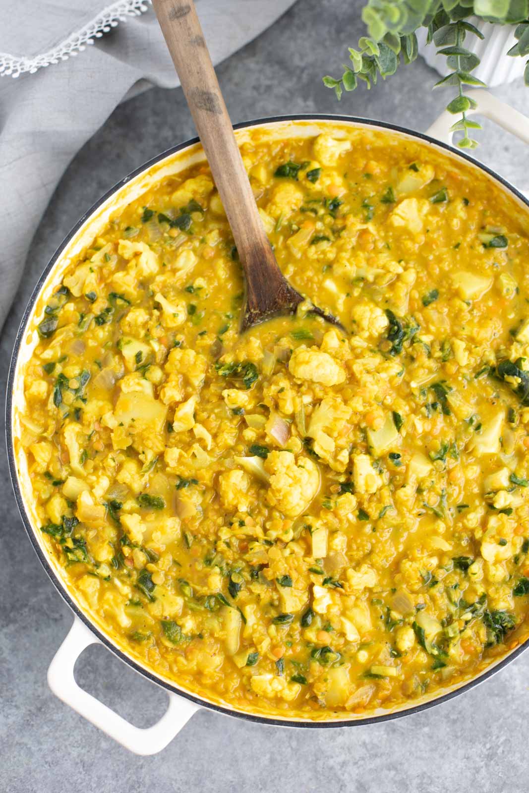 A large white pan filled with yellow Thai curry, vegetables, and a wooden spoon.