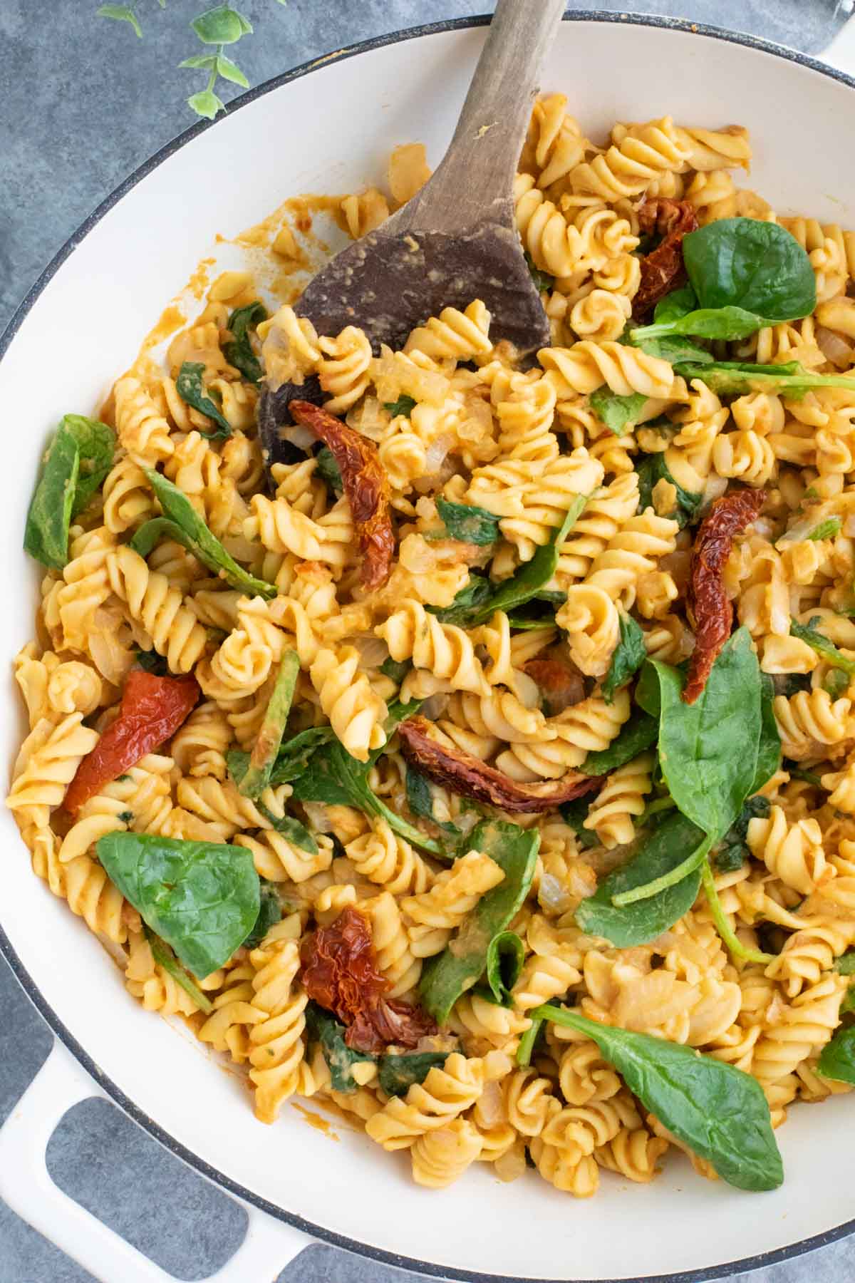 A white skillet filled with vegan pasta, sun-dried tomatoes, and spinach. 
