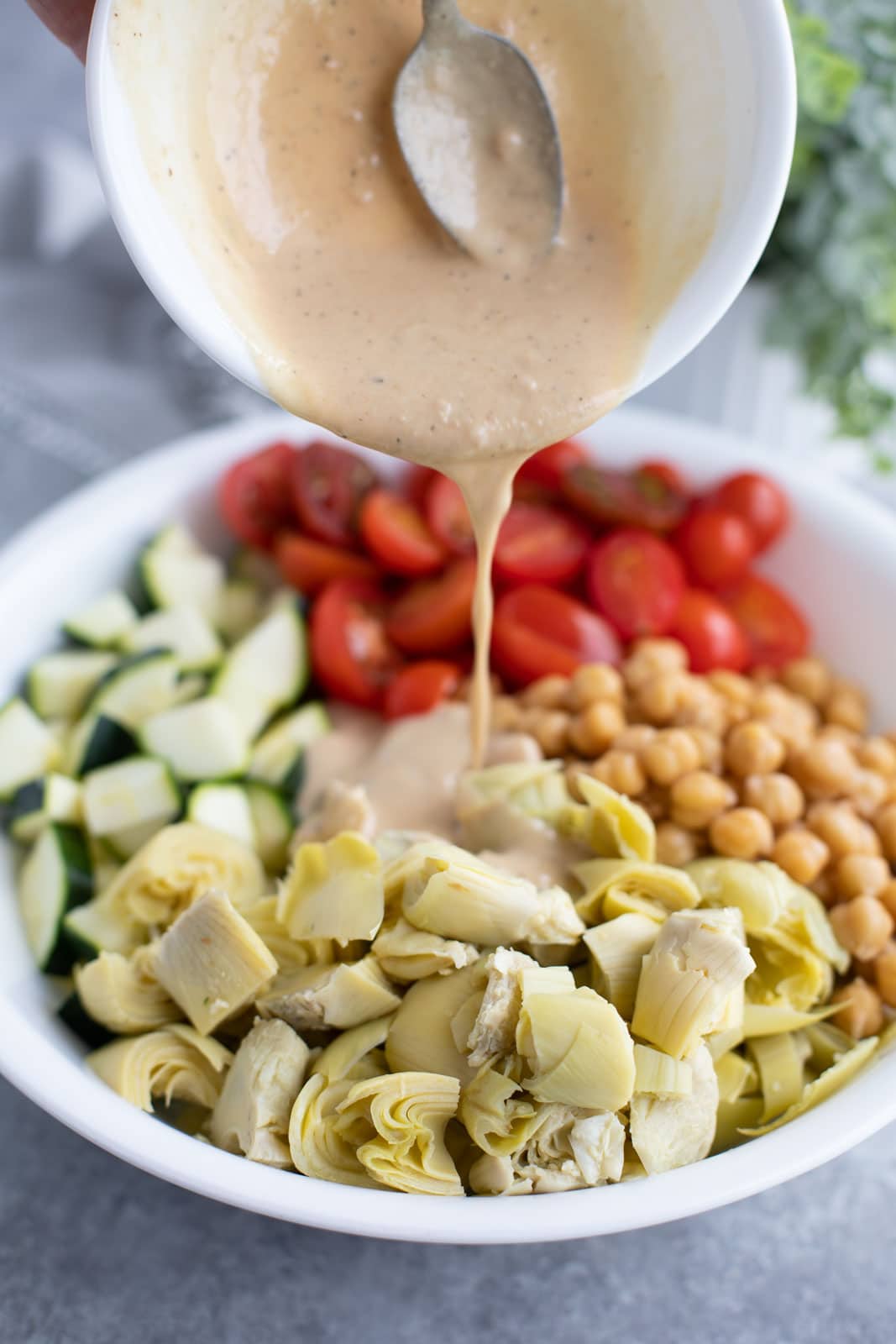 Sauce being poured out of a small bowl over a large bowl of vegetables. 