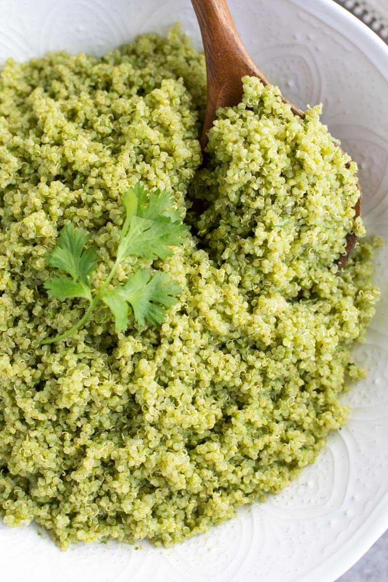 A wooden spoon scooping quinoa out of a large white bowl.