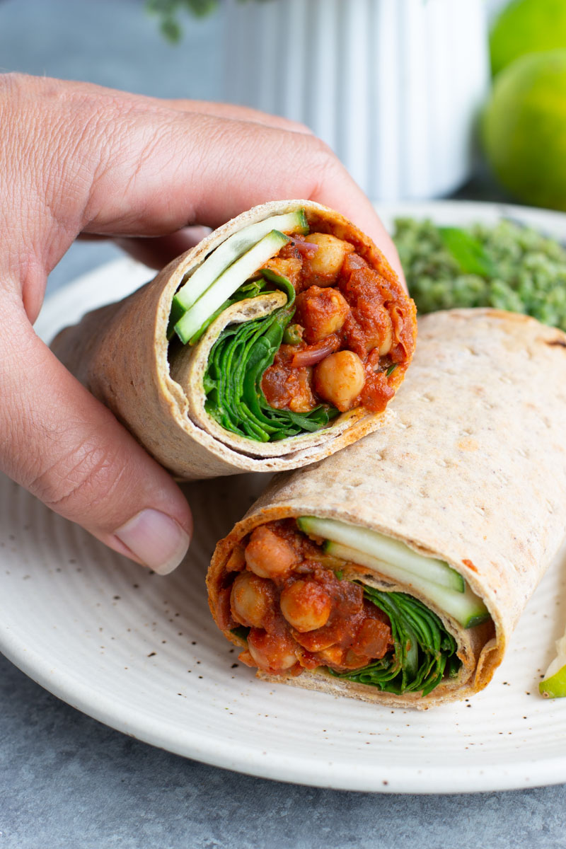 A hand grabbing half of a chickpea lavash wrap that's stacked on top of the other half on a white plate. 