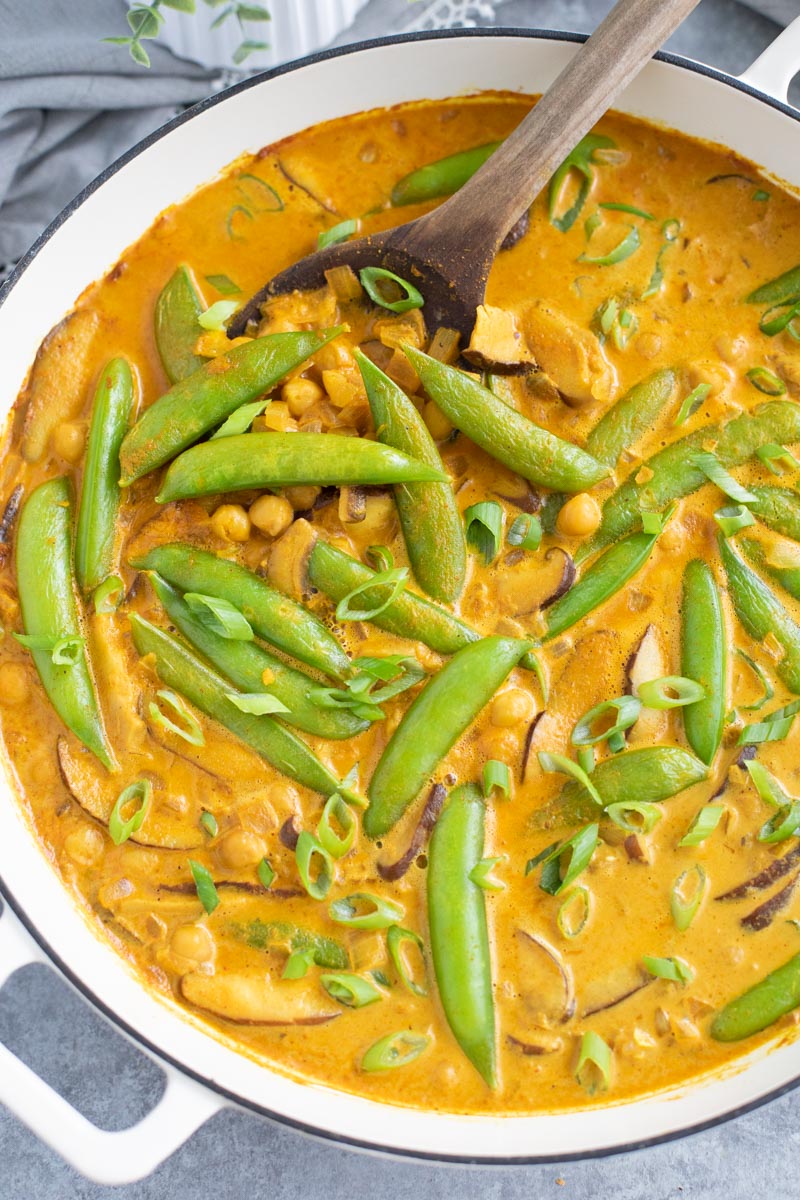 A large white pan filled with snap peas, chickpeas, and mushrooms in sauce. 