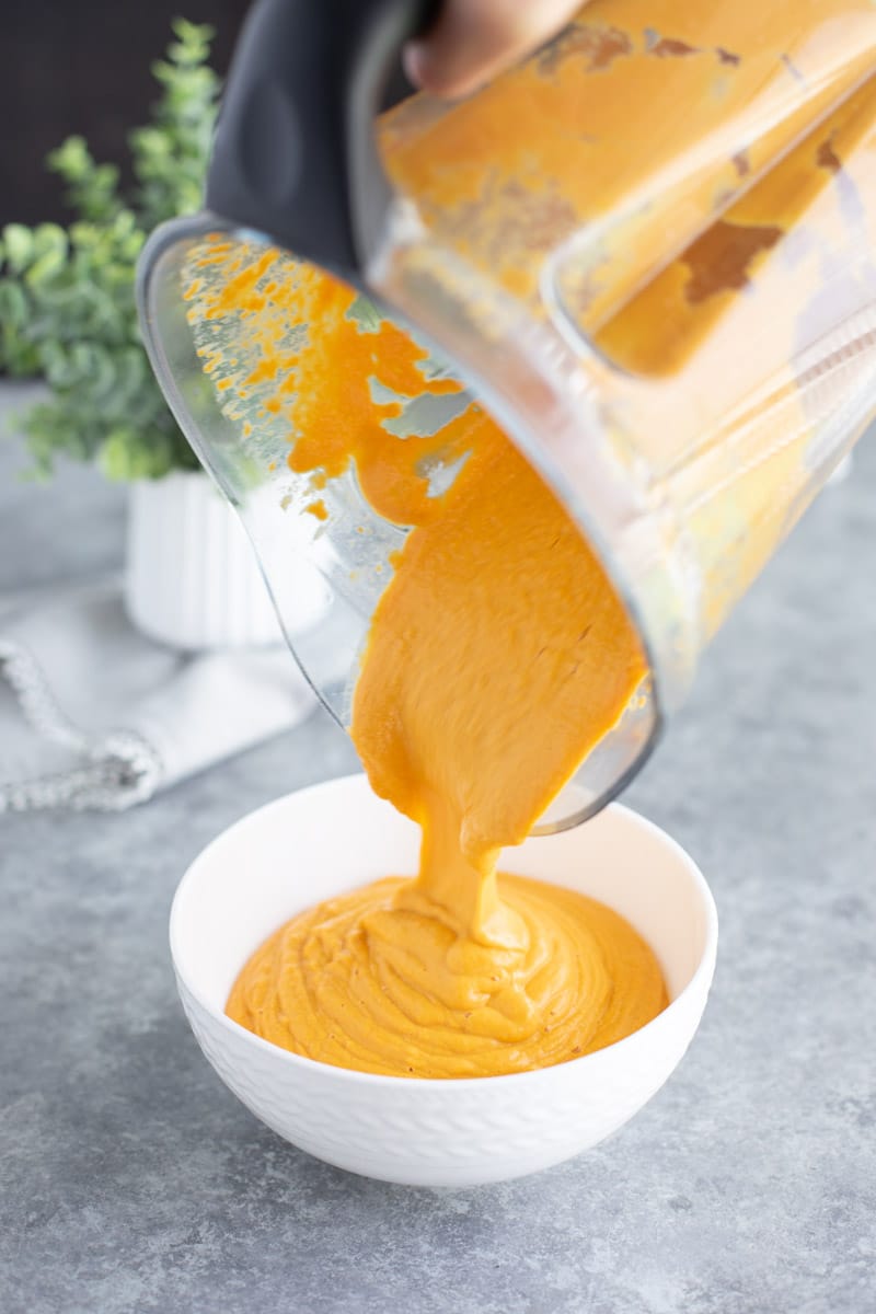 A hand pouring the contents of a blender into a white bowl on a gray background.