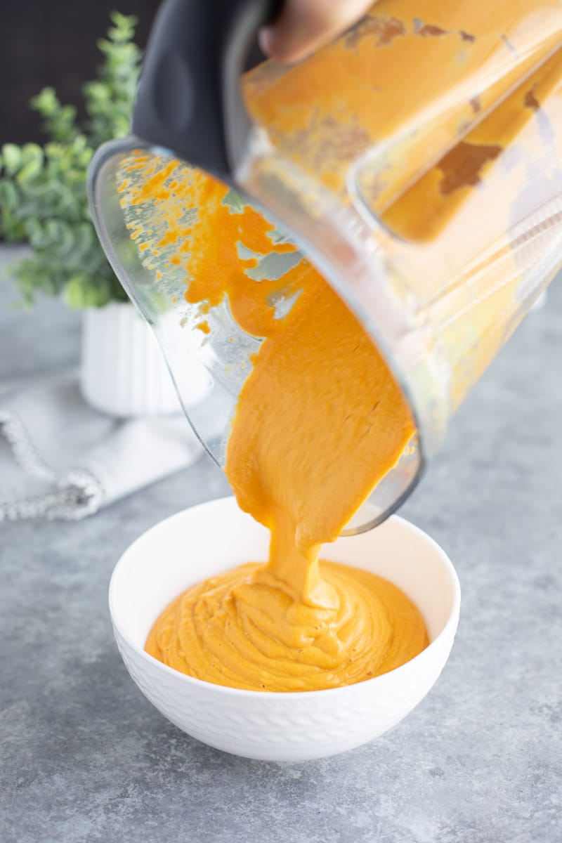 A hand pouring the contents of a blender into a white bowl on a gray background. 