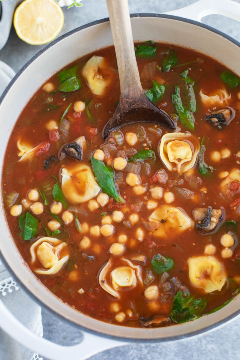 A wooden spoon in a white dutch oven filled with soup on a gray background.