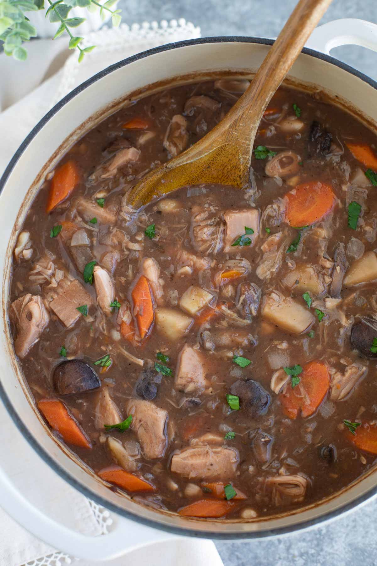 A large white pot filled with vegan beef stew in a large white pot on a gray background.