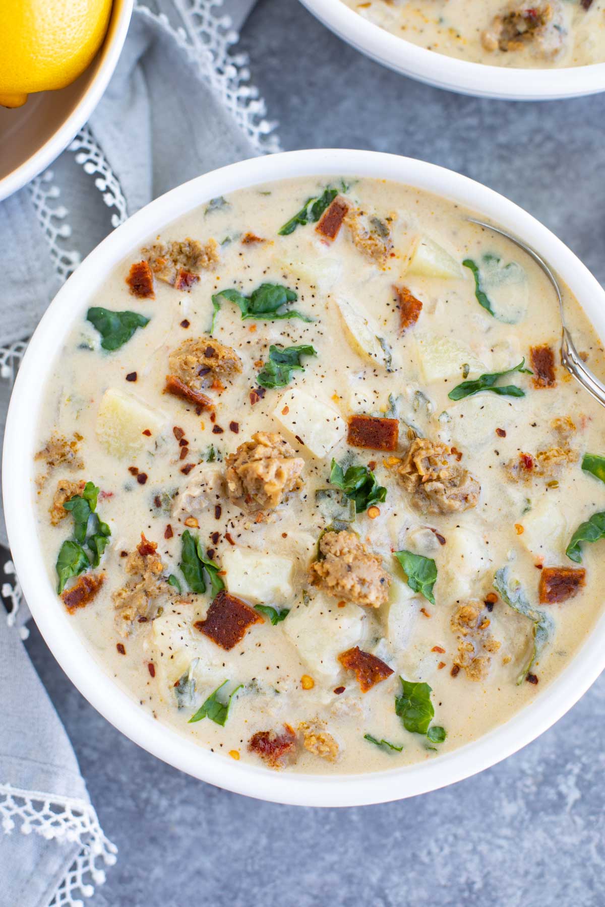 A white bowl filled with zuppa toscana and a spoon on a gray background.