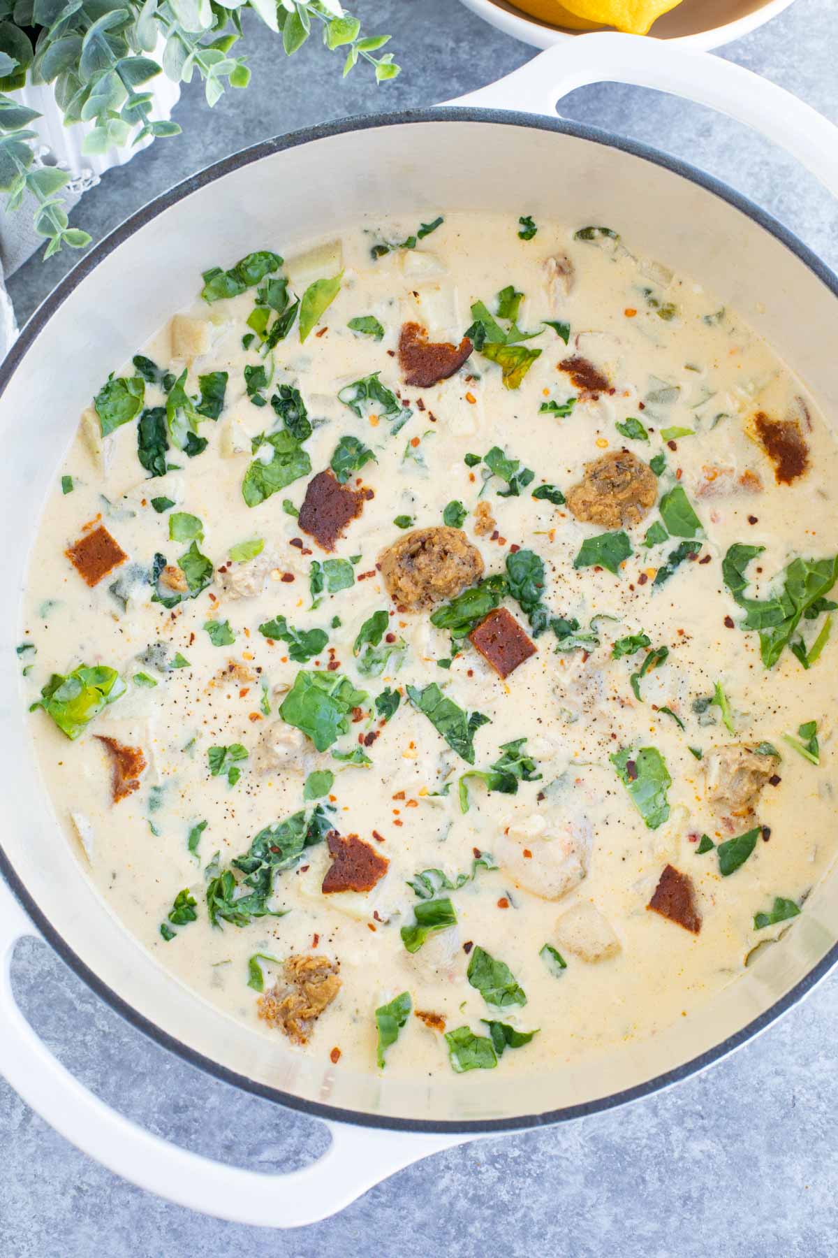 A large white dutch oven filled with vegan zuppa toscana on a gray background.
